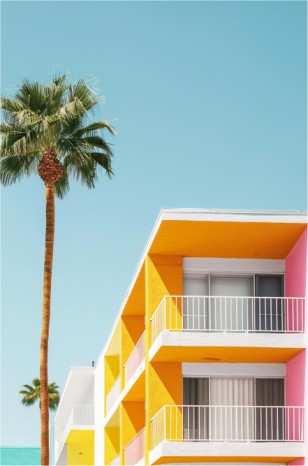 A vibrant architectural scene with pink and yellow buildings, a palm tree, and a clear blue sky, creating a striking and serene tropical ambiance.