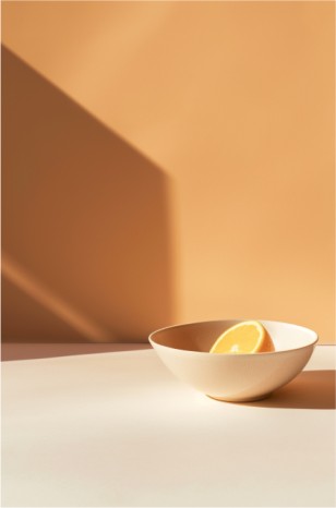 A minimalist composition featuring a white bowl with a vibrant orange slice and geometric shadow.