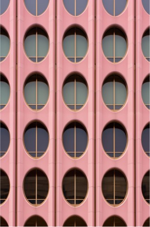 A building facade features a unique design with round windows in squared borders, creating a rhythmic pattern in soft pink and gold hues.