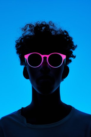 A person's silhouette stands out against a vibrant blue background, neon pink sunglasses drawing attention.